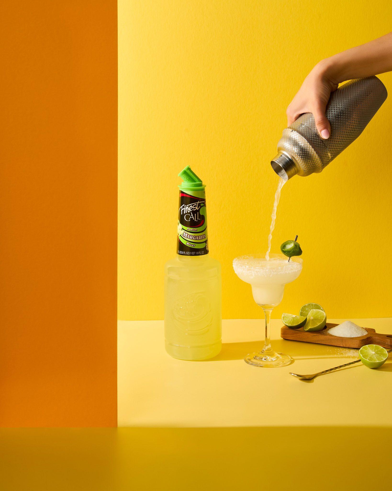Cocktail being poured over a fresh margarita with lime garnishes
