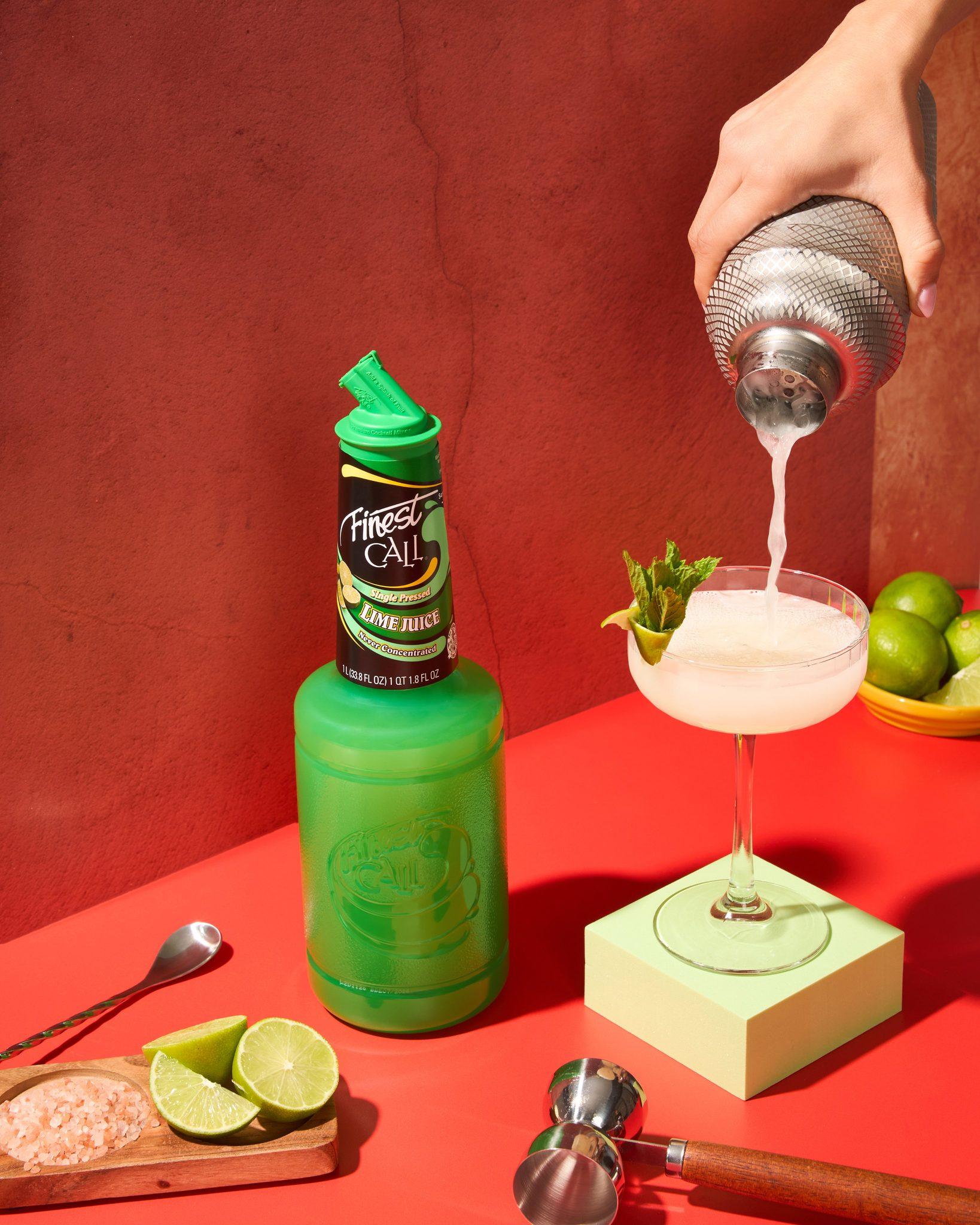 Finest Call Lime Juice bottle being mixed into a cocktail