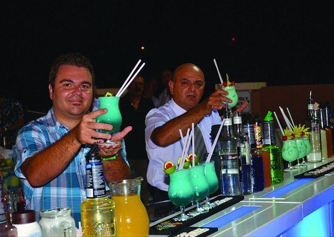 Two bartenders pouring cocktails side by side at a competition bar